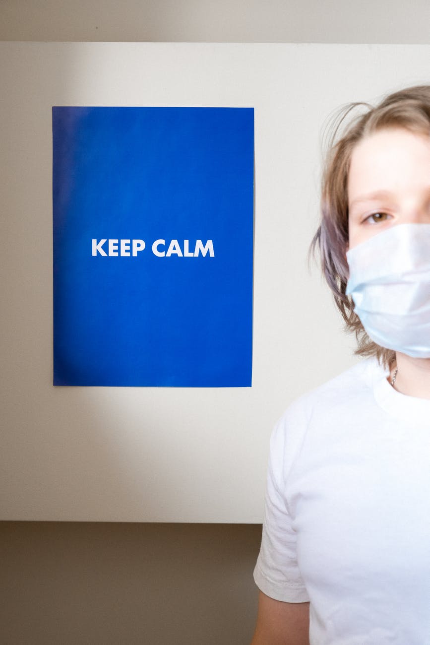 woman in white crew neck t shirt and face mask standing near a keep calm slogan